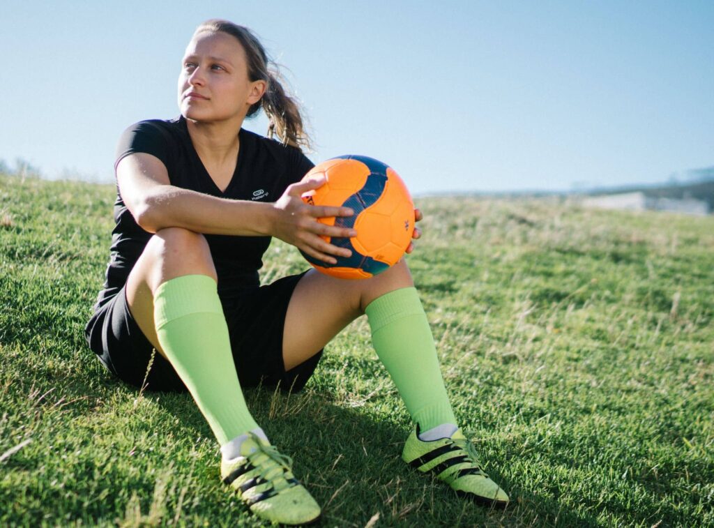 Fotbollsspelare som sitter med en boll på en gräsplan i kvällsljus